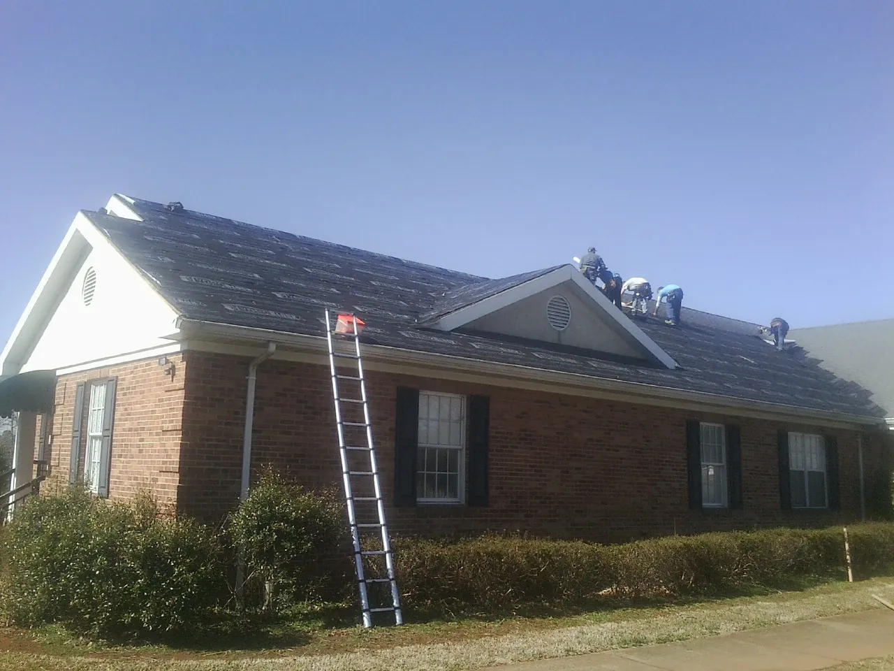 Crew tearing shingles off a brick ranch roof with a ladder set — Emergency Roof Repair work by our crew in Pound Ridge