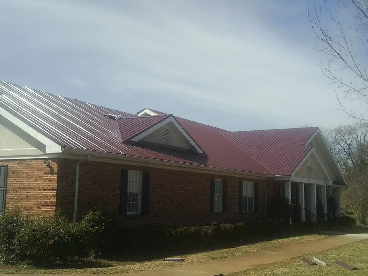 Red metal roof with gabled entries on a long brick building, from a Hail Damage Roof Repair job in Pound Ridge