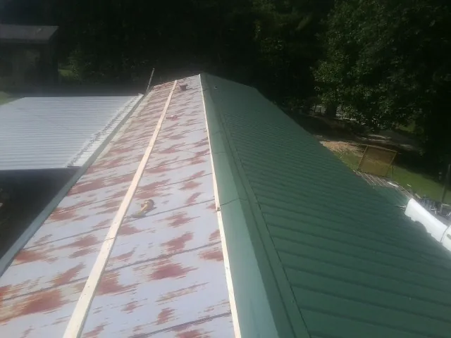 Old rusted panels beside newly installed green metal roofing — Wind Damage Roof Repair by Roofing Brothers in Pound Ridge