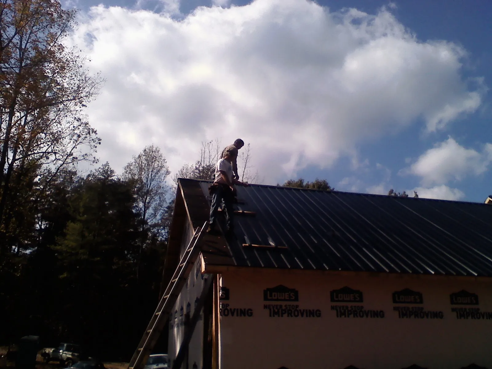 Roofer fastening dark metal panels high against a cloudy sky, from a Roof Inspection job in Pound Ridge