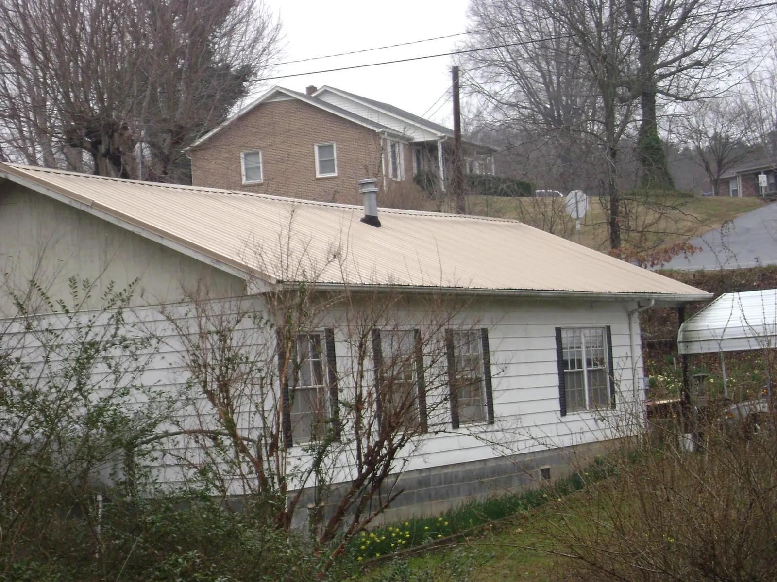Tan metal roof on a white sided house set into a hillside — Commercial Roofing by Roofing Brothers in Pound Ridge