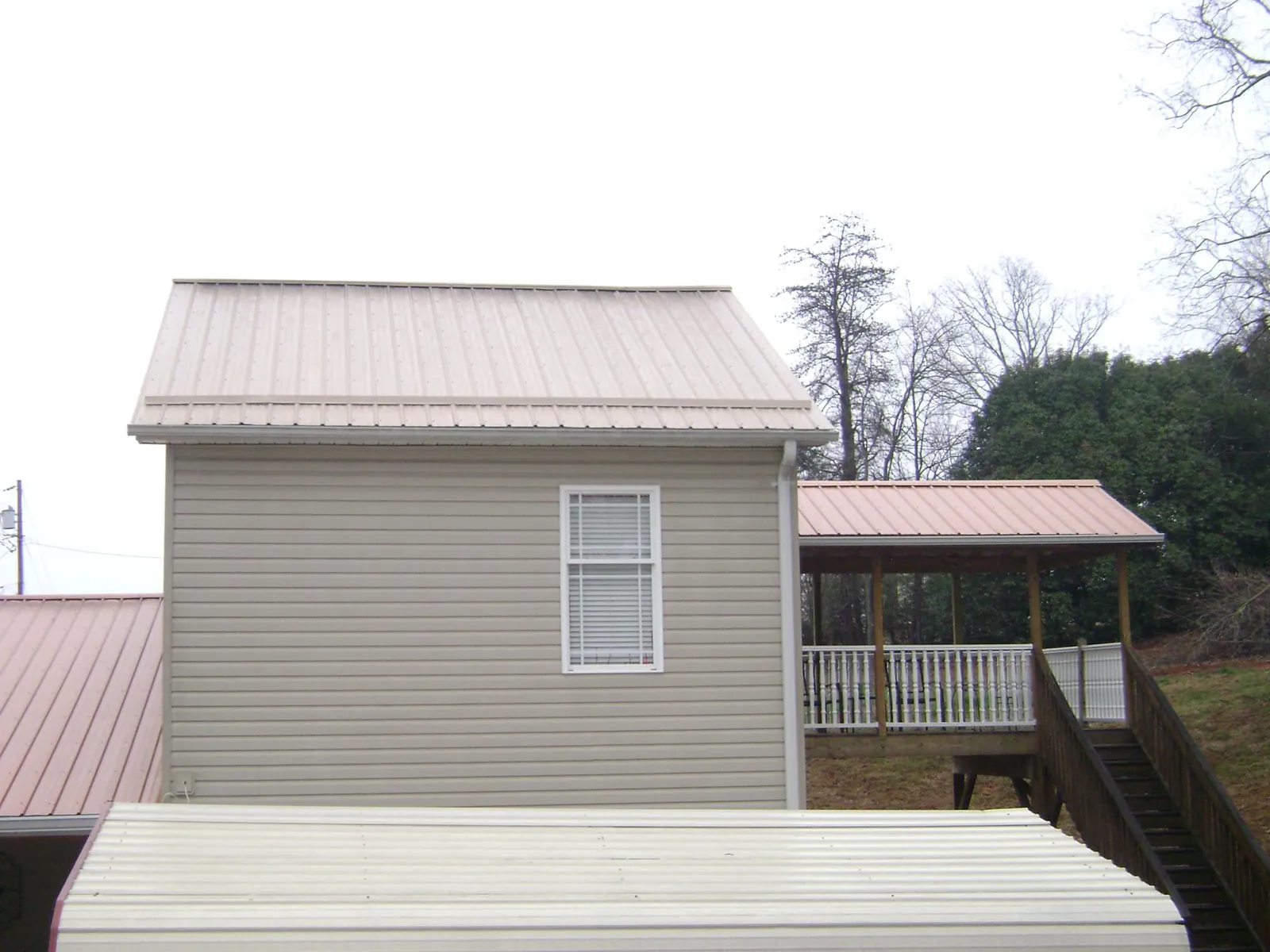 Tan metal roofs on a two story addition and attached porch, from a Roof Replacement job in Pound Ridge